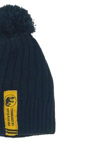 Marine gebreide beanie met een pompon bovenop en een gele label met een dinosaurusafbeelding en tekst, met ribbeltextuur door het hele ontwerp.