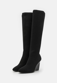 Knee-high mustad kollaste kõrgusega mustad platvormsaapad, mis on valmistatud tekstuuriga kangast, millel on sujuv terav nina ja soonikkoes varrukas ülaosas.