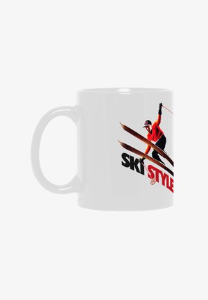 Weiße Tasse mit einem Skifahrer in orangefarbener Jacke und schwarzer Hose, der mit gekreuzten Skiern in der Luft springt, darüber der fettgedruckte Text "SKI STYLE" in Schwarz und Rot.