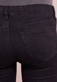 Los vaqueros de mezclilla negra presentan un estilo ajustado, bolsillos traseros con un diseño de logo distintivo bordado y una textura suave.
