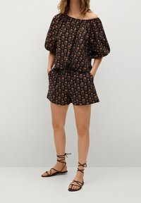 Musta olkaimeton paita kukkakuviolla, yhdistettyinä matching-shortsien kanssa. Kevyt kangas, rento istuvuus ja ruskeat remmisandaalit.