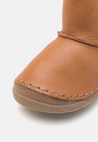 Bota de cuero marrón con punta redondeada, costuras visibles y suela texturizada. Material flexible y superficie lisa con un diseño casual.