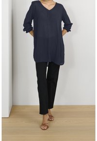 Marineblå V-hals tunika med trekvartlange ærmer, løs pasform, tekstureret stof, kombineret med sorte bukser med lige ben og brune sandaler med stropper.