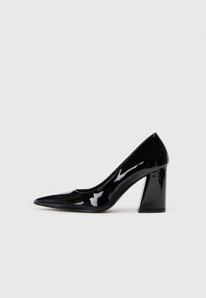 Chaussure à talon haut en vernis noir avec un embout pointu et un talon épais, présentant une texture lisse et brillante ainsi qu'un design élégant.