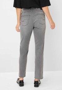 Jeans in denim grigio con taglio dritto, dotati di tasche posteriori con cuciture curve. Indossati con scarpe nere, su uno sfondo semplice.