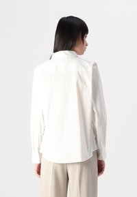 Witte button-up blouse met lange mouwen, gladde textuur, achterste plooi en afgeronde zoom. Draag het met beige hoge taillebroek.