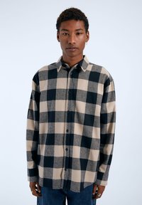 Camisa de manga larga con botones en un gran patrón de cuadros beige y negro, hecha de una tela suave, con cuello puntiagudo y botones en la parte delantera.