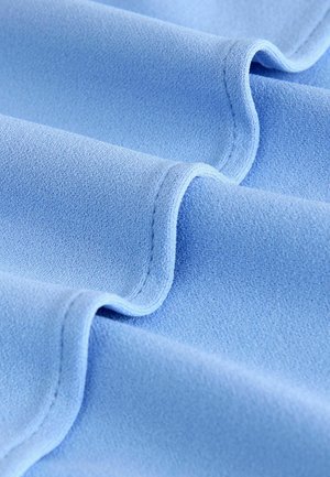 Vaaleansininen kangas, jolla on sileä pinta, pehmeät, virtaavat laskokset ja hienovaraiset ompelutiedot reunoilla.