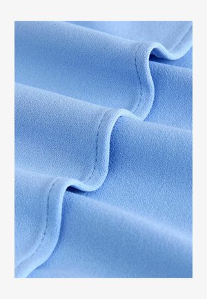 Ljusblått tyg med en slät textur, som har mjuka, flödande veck och subtila sömdetaljer längs kanterna.