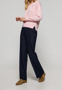 Light pink knitted sweater with a v-neck, paired with dark blue wide-leg trousers. Brown loafers complete the outfit.