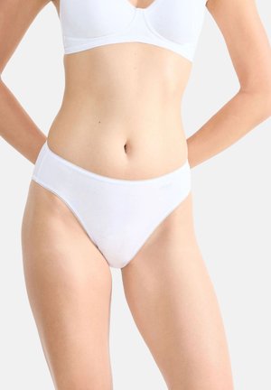 Femme portant un soutien-gorge blanc uni et un slip en coton blanc assorti, de style bikini, sur un fond clair uni.