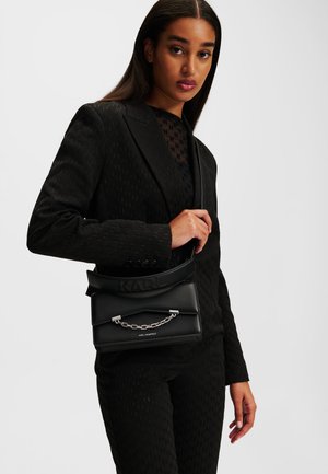 Black handbag with a structured shape, textured finish, and a silver chain detail. Features a logoed strap and a flap closure.