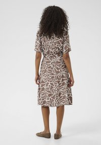 Brown dress with white abstract pattern, short sleeves, and cinched waist. Worn with brown flat shoes, viewed from the back.