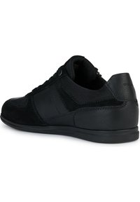 Zapatilla baja negra con parte superior de cuero y tela mezclados, cierre con cordones y suela de goma texturizada, vista desde un ángulo posterior lateral.