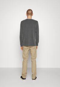 Šedý top s dlouhými rukávy, bavlněný materiál, pohodlný střih. Spárovaný s béžovými kalhotami, rovný střih, a černými slip-on botami.