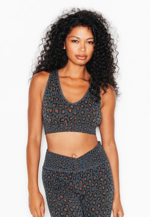 Donna con capelli ricci che indossa un reggiseno sportivo e leggings abbinati con stampa leopardata grigio scuro, in piedi contro uno sfondo bianco.