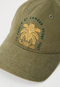 Olíva zöld pamut sapka ívelt karimával, sárga pálmafás hímzéssel és teal színű felirattal, kiemelve a különleges dizájnt.