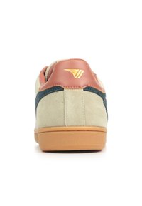 Suède sneakers met een beige bovenkant, teal accenten en een bruine leren hieltab met een gouden logo. Rubberen zool, minimalistisch ontwerp.