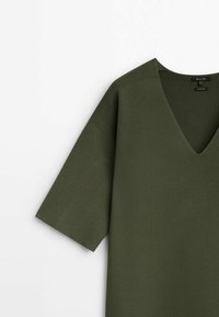 Olive green v-neck top, short sleeves, made of textured fabric. Simple design with a relaxed fit, no visible patterns or accents.