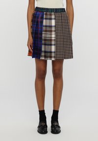 Falda corta de cuadros con una mezcla de patrones en azul, marrón y naranja; presenta una cinturilla elástica y un diseño plisado; se lleva con mocasines negros.