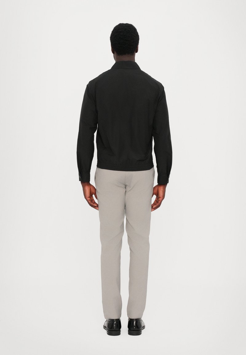 Black jacket with a collar, zip closure, and elastic cuffs, paired with light gray pants and black shoes. Viewed from the back.