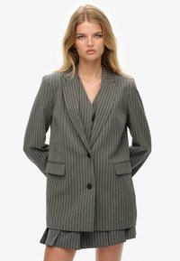 Blazer gris con rayas de tiza, con solapa muesca, cierre de un botón, dos bolsillos frontales y un corte relajado, estilizado sobre un conjunto a juego.