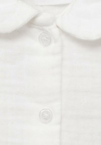Camicia bianca in cotone con colletto rotondo e una fila di due bottoni trasparenti. Il tessuto è leggermente testurizzato con una trama leggera.