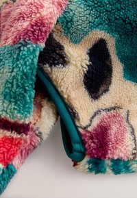 Nahaufnahme eines mehrfarbigen Fleece-Stoffs mit abstrakten Mustern in Türkis, Pink, Creme, Schwarz und Rot, die Struktur und Nähte zeigt.