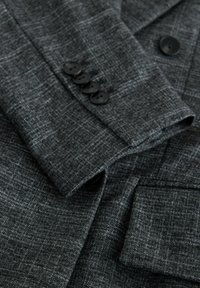 Grijze textuur blazer met een subtiel patroon. Heeft vier zwarte knopen op de manchetten en een enkele voorkant zak. Glad stoffen afwerking.