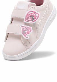 Baskets PUMA en matériau synthétique rose doux avec deux bandes Velcro. Présente des appliqués en forme de papillon rose et argent. Semelle en caoutchouc blanche.