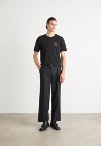 Zwarte katoenen T-shirt met een rode "HUGO" logo op de borst, gecombineerd met hoge zwarte broek en zwarte leren schoenen.