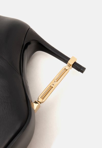 Chaussure à talon haut noire avec un talon stiletto fin, dotée d'un support décoratif en métal doré gravé des lettres D2.