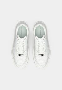 Par hvite snøresko med perforerte tåhetter og "KARL LAGERFELD" trykket på innleggssålene, vist ovenfra på hvit bakgrunn.