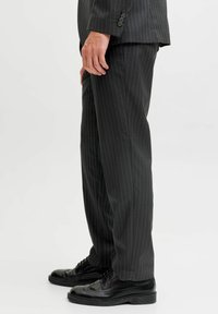 Czarne spodnie w prążki wykonane z gładkiej tkaniny, o prostym kroju, z bocznymi kieszeniami i kantem z przodu, zestawione z czarnymi butami.