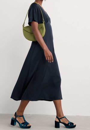 Robe midi bleu marine avec manches courtes évasées, coupe décontractée. Sac à main vert incurvé et sandales à plateforme en velours bleu sarcelle avec talons blocs.