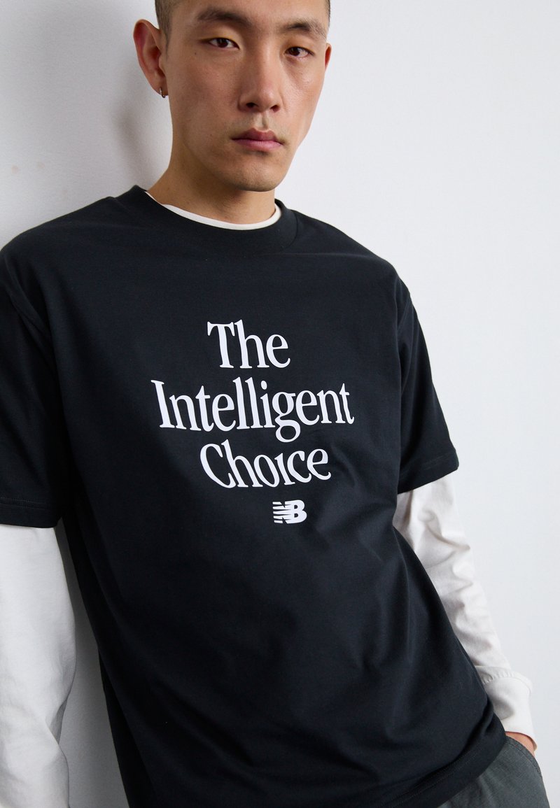 Schwarzes T-Shirt mit dem Text "Die intelligente Wahl" in Weiß. Enthält ein kleines weißes New Balance-Logo unten. Kurze Ärmel, aus Baumwolle.