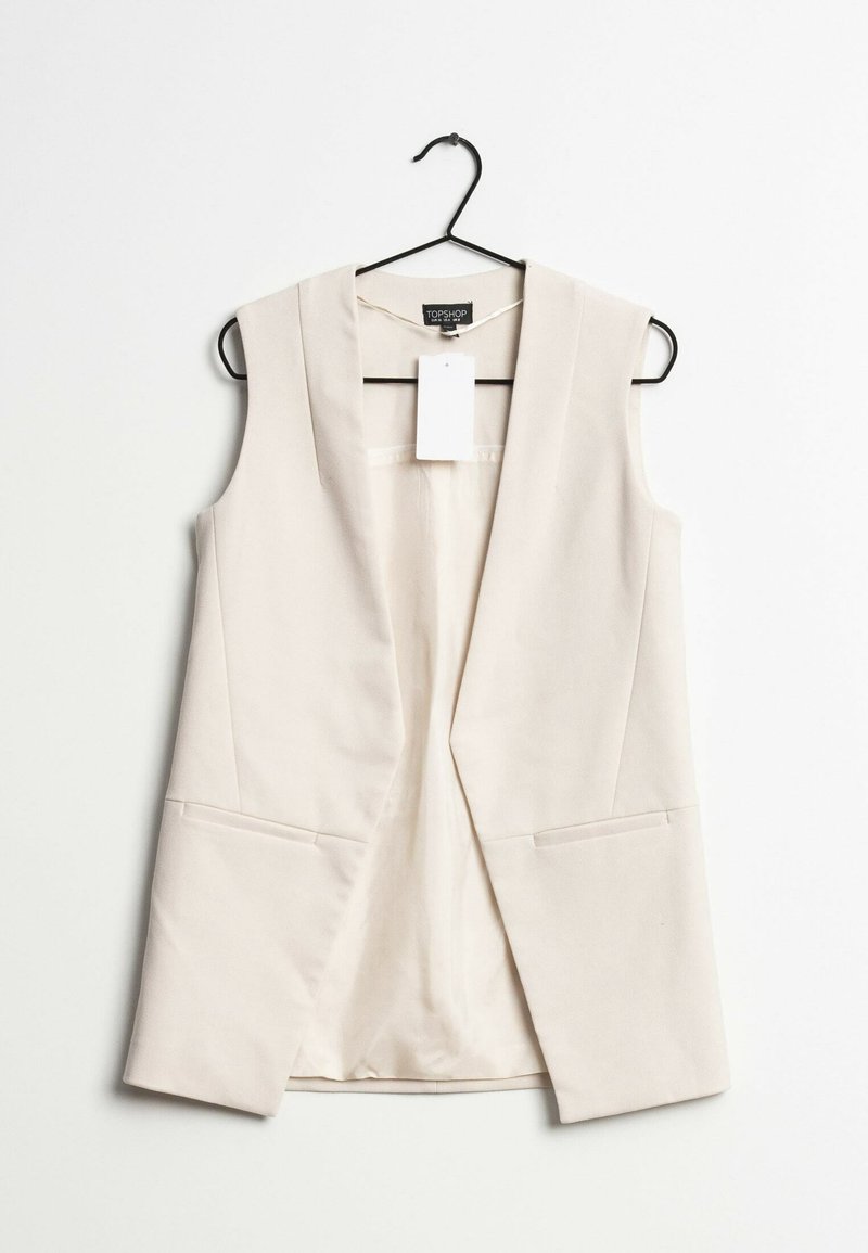 Blazer sans manches beige clair avec un col cranté, deux poches avant et une étiquette suspendue. Texture lisse et design ajusté.