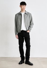Szürke kockás bomber dzseki fehér környakú pólóval, fekete farmernadrággal és fekete cipővel. Slim fit dizájn, sima textúra, elasztikus mandzsetták.