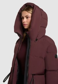 Chaqueta acolchada burdeos con una gran capucha, cierre de cremallera y cordones, con una textura brillante y acentos de hardware negro.