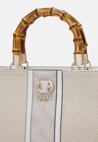 Beige handbag with a textured finish, featuring a bamboo handle and gold hardware. Displays a monogram pattern and a logo plaque on the front.