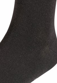 Calcetín negro de canalé hecho de material suave, con una textura lisa y talón ligeramente reforzado. Vista en primer plano de la trama de la tela.