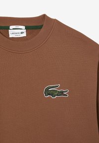 Felpa marrone con colletto a costine, caratterizzata da un logo di coccodrillo ricamato in verde e rosso sul lato sinistro del petto e tessuto strutturato.