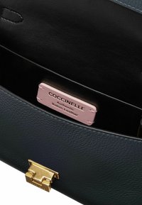 Interno della borsa in pelle Coccinelle, con pelle nera testurizzata, chiusura in metallo dorato e un'etichetta in pelle rosa con la dicitura "Pelle Italiana Autentica".