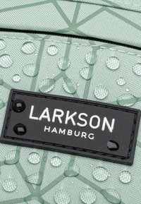 Tessuto verde a motivo con gocce d'acqua; presenta un'etichetta nera con testo bianco "LARKSON HAMBURG" e dettagli curvi neri.