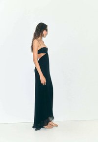 Vestido maxi negro con tirantes finos y corte lateral. Hecho de una tela ligera, presenta una silueta fluida y una textura suave.