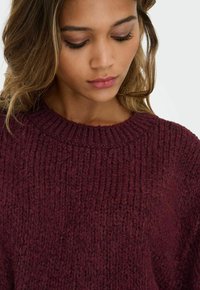 Maglione lavorato a maglia color bordeaux con scollatura a girocollo a coste. Presenta un motivo a maglia grossa e testurizzata. Tessuto morbido con vestibilità comoda.