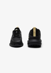 Czarne buty sportowe wykonane z mieszanki zamszu i siateczki, z teksturowanymi sznurówkami, wyraźnym logo i kontrastującymi złotymi akcentami na pięcie.
