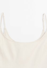 Haut camisole beige avec fines bretelles réglables, tissu à texture lisse et encolure arrondie. Comprend des détails discrets de couture sur les côtés.
