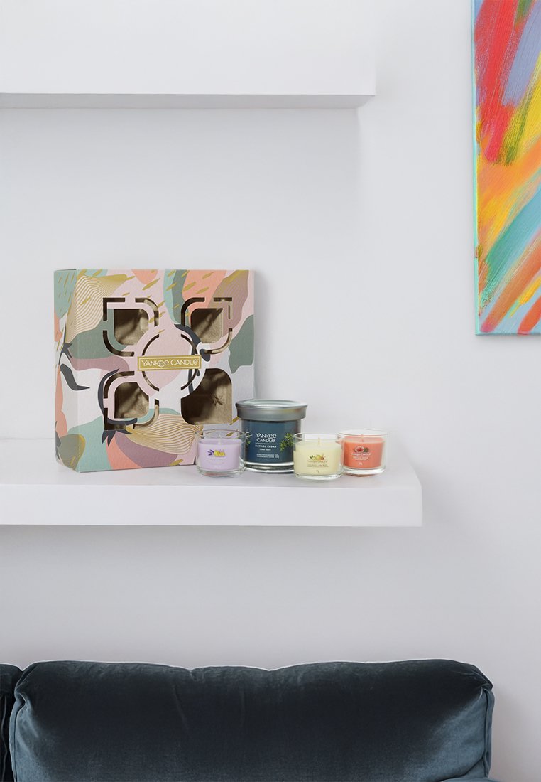 Zestaw prezentowy Yankee Candle w wzorzystym pudełku z wycięciami, zawierający cztery szklane świece w kolorze lawendy, żółtym, pomarańczowym i zielonym.