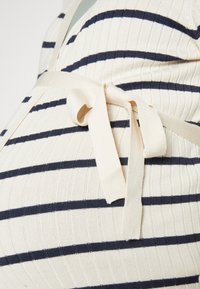 Randig stickad topp i kräm och marinblå, med en omslagsdesign och knytstängning som framhäver texturen genom ribbat tyg.